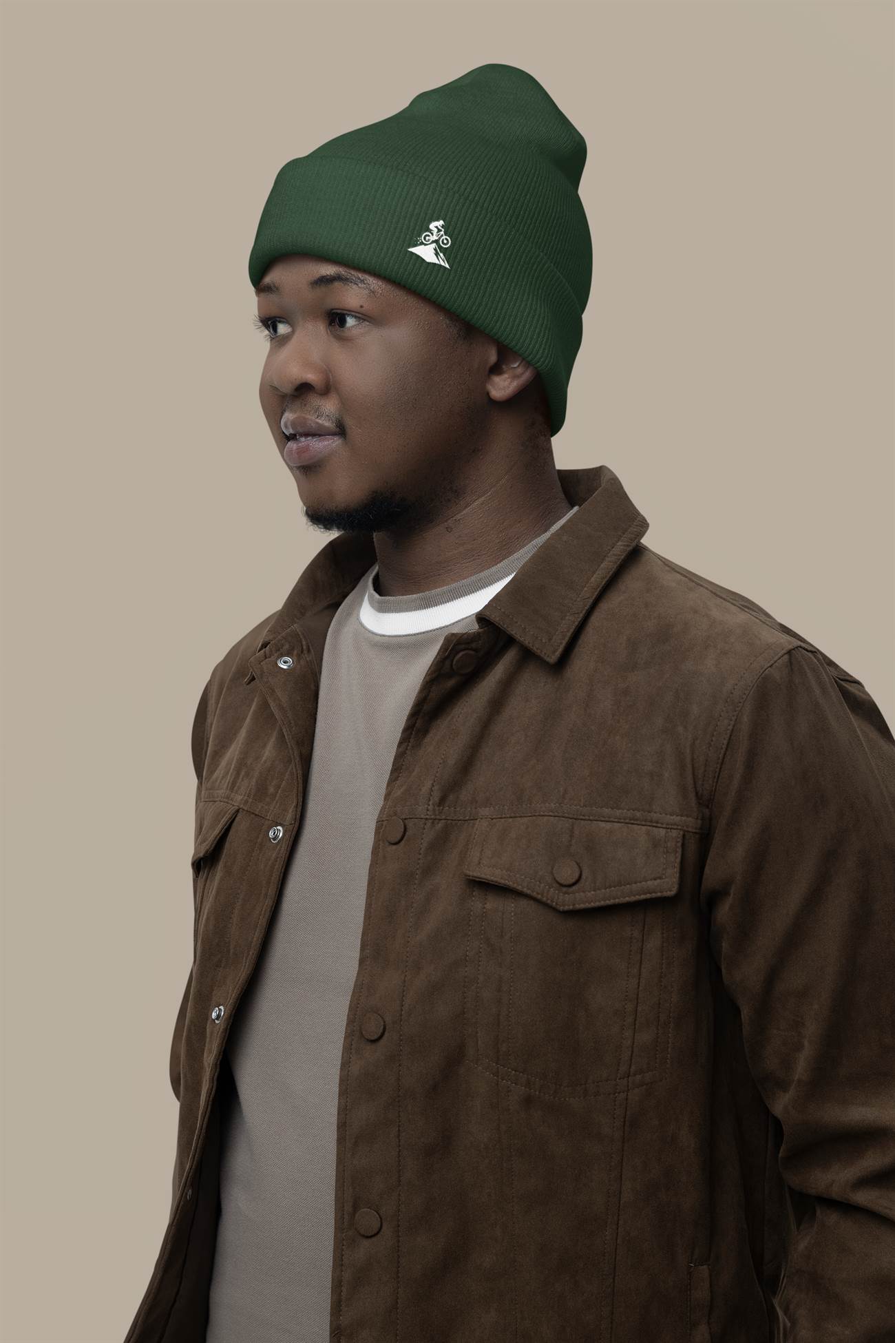 Green Madeira Beanie with embroidered mountain bike logo, worn by a man in a brown suede jacket. A perfect blend of style and warmth.
