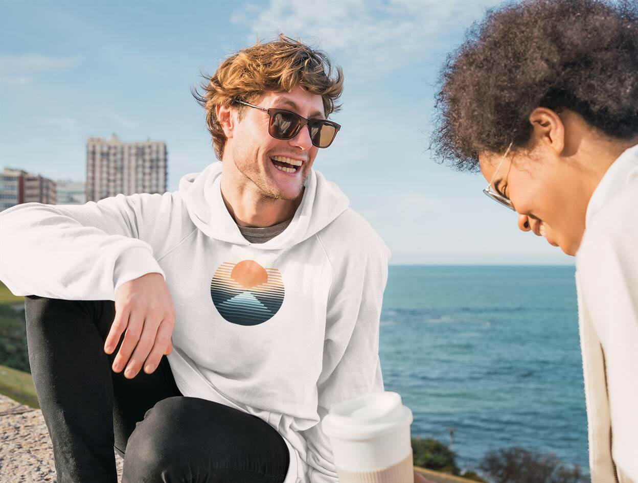 White Nazaré vintage hoodie with a sunset design, worn by a man enjoying a seaside view. Comfortable and sustainable surf-inspired fashion.