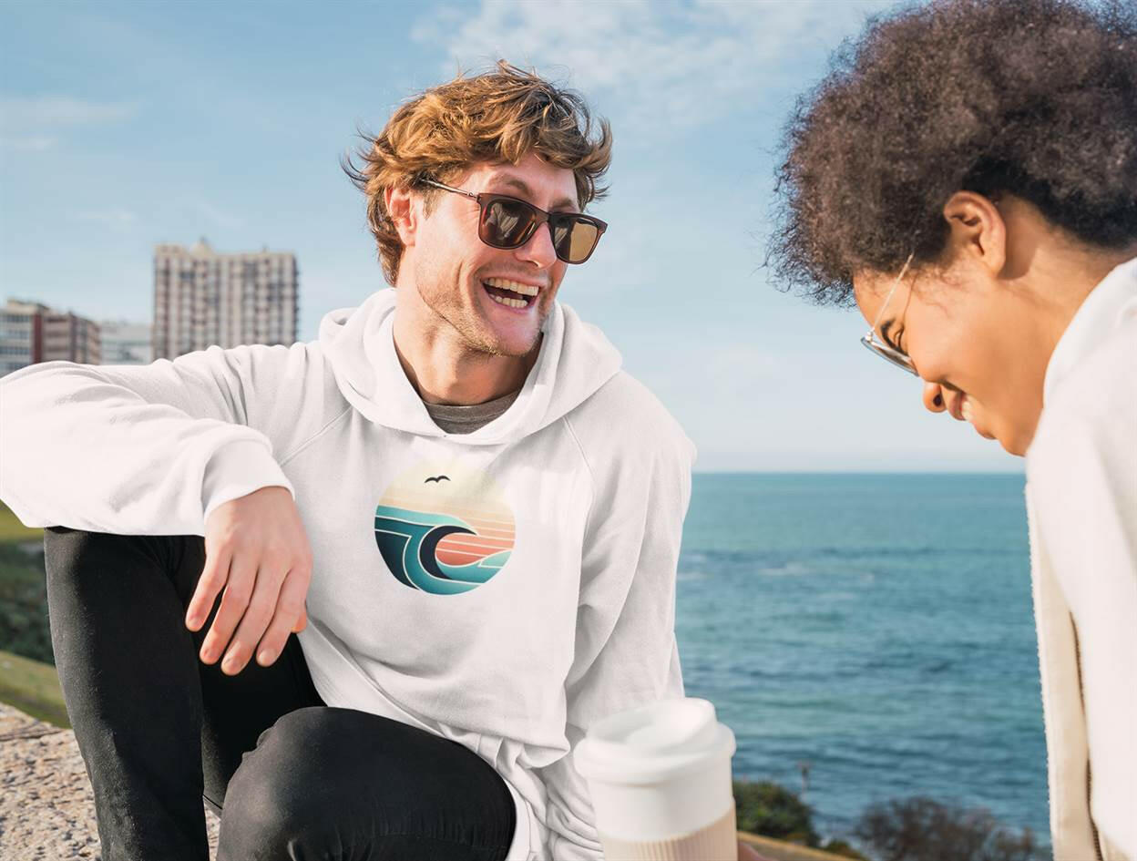White Nazaré Surf Wave Hoodie worn by a man by the sea. Vintage surf-inspired design with organic cotton for sustainable fashion.