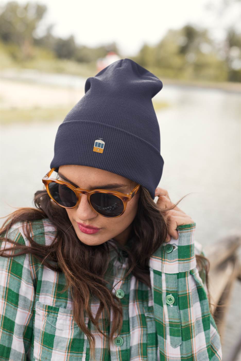 Navy blue Lisbon Electrico Beanie with embroidered tram detail, styled with sunglasses and a plaid shirt. A warm and stylish turbo acrylic hat.