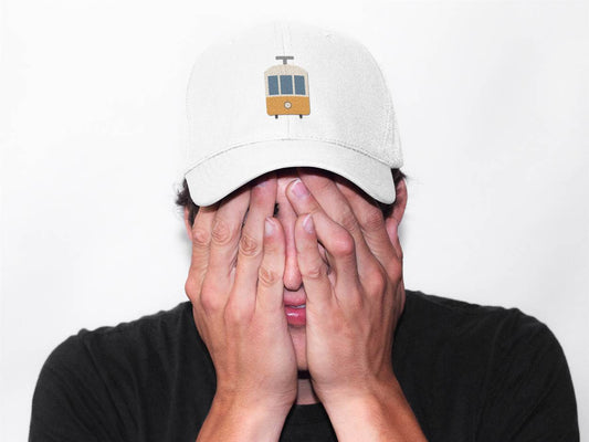 Unisex Lisbon Tram Cap with minimalist embroidered tram logo in white, worn by a man covering his face. A stylish tribute to Lisbon's heritage.
