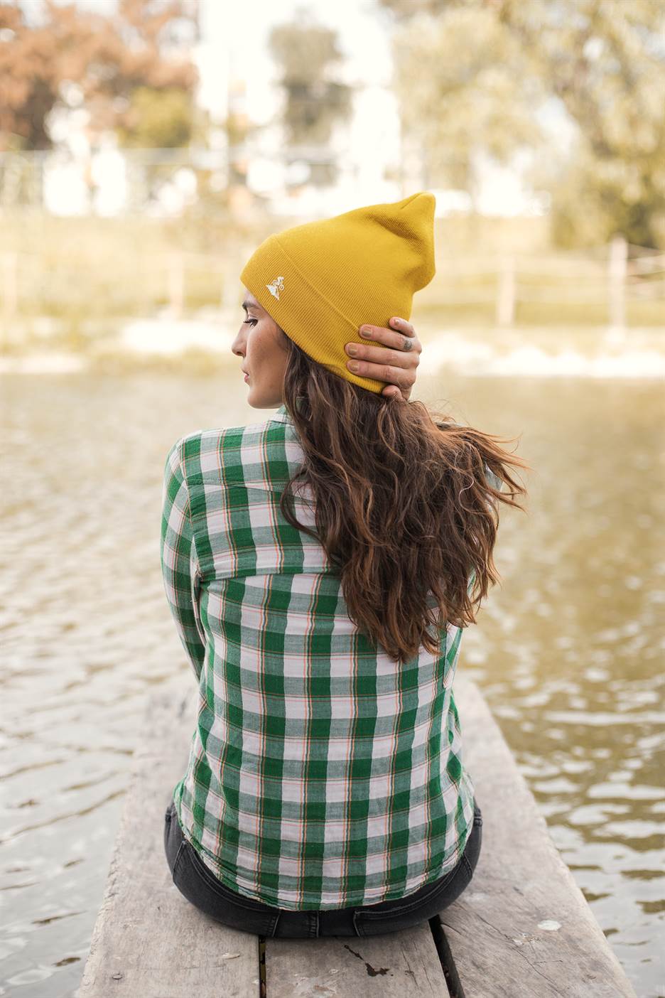 Yellow Madeira Beanie with embroidered mountain bike logo, worn by a woman sitting on a dock. A vibrant and cozy choice for outdoor lovers.